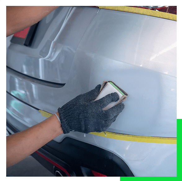Person polishing car bumper with sandpaper.